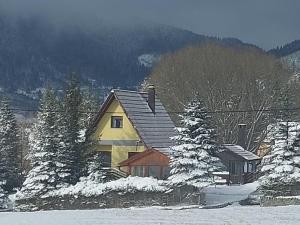 a yellow house in the snow with trees at Kuća za odmor VITICA s vanjskim kaminom in Kupres