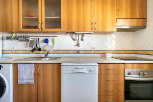 a kitchen with wooden cabinets and a white dishwasher at Fantástico T2 AC Wi-FI e TV Cabo 2WC Toalhas e Lençóis in Altura