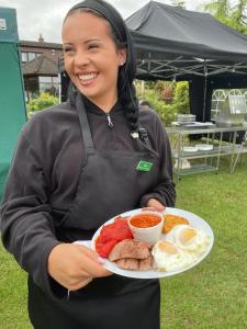 a woman is holding a plate of breakfast food at Silvestone Farm Campsite in Silverstone