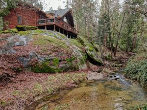 uma casa na floresta com um riacho em frente em Exquisite Log Cabin in the Pines and Very Private em Sonora