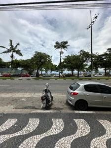a motorcycle parked next to a car on a street at Kitnet em frente a praia de Santos in Santos