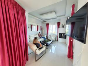a woman sitting on a couch in a living room with red curtains at Centaur Villa in Agios Ioannis Pelio