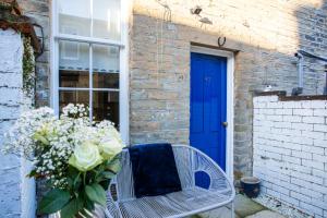 een vaas met bloemen op een stoel met een blauwe deur bij Cosy 2 bedroom Cottage in a World Heritage Village in Shipley
