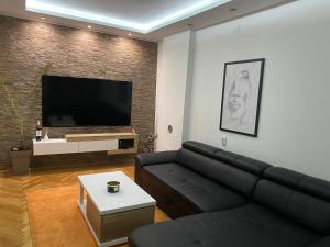 a living room with a black couch and a flat screen tv at Regal Comfort Apartment in Pirot