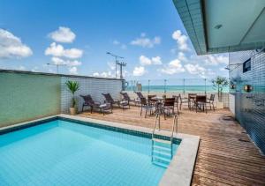 a swimming pool with chairs and a table and the ocean at Flat para 2, de frente para o Mar in Natal