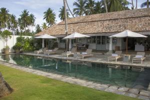 una casa con piscina con sillas y sombrillas en Samudra Beach House, en Habaraduwa Central