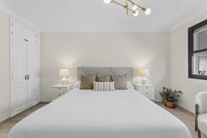 a white bedroom with a large white bed and two lamps at Casahost Guenia Beach Apartment in Arrecife
