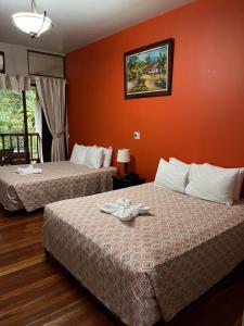 2 camas en una habitación de hotel con paredes de color naranja en Hotel El Bambu, en Sarapiquí