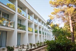 un bâtiment blanc avec des arbres devant lui dans l'établissement Hotel Kimen - Annex, à Cres