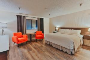 ein Hotelzimmer mit einem Bett und zwei orangefarbenen Stühlen in der Unterkunft Hotel International in Lynnwood