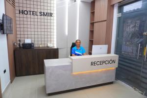 a woman sitting at a reception desk with a laptop at Hotel SMIR in Huaquillas