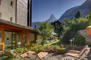 un patio con sillas, mesas y montañas de fondo en Hotel Metropol & Spa Zermatt, en Zermatt