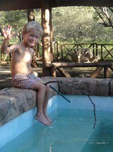a young boy sitting on the edge of a swimming pool at Les 3 Marulas in Marloth Park