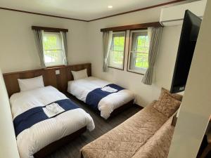two beds in a room with a couch and a tv at Kiyosatokogen Country Inn The Classic in Hokuto