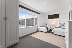 a white bedroom with two beds and a window at Belle Escapes - Bountiful Family Oasis in West Beach in Henley Beach South