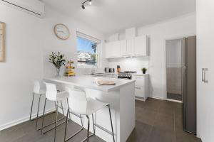a white kitchen with a white counter and stools at Belle Escapes - Bountiful Family Oasis in West Beach in Henley Beach South