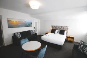 Batemans Bay Lodge في خليج بايتمانس: غرفة فندقية بسرير وطاولة وكراسي
