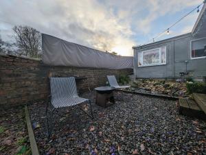 un patio trasero con 2 sillas, una mesa y una pared en The Cabin en Bonnybridge