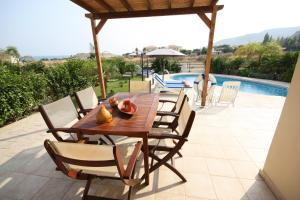 a wooden table and chairs on a patio with a pool at SeaView Villas in Pissouri