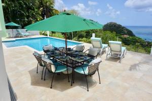 una mesa con sillas y una sombrilla junto a la piscina en Lovely 3 BR Ocean View Villa, en Cap Estate
