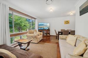 ein Wohnzimmer mit einem Sofa, Stühlen und einem Tisch in der Unterkunft Azalea Cottage, Leura NSW Australia in Leura