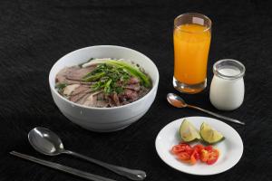 a table with a bowl of food and a glass of orange juice at Brilliant Me Tri Hotel & Spa in Hanoi