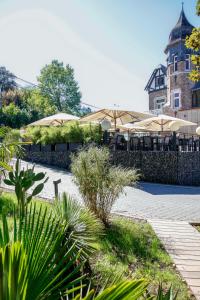 un patio con mesas y sombrillas frente a un edificio en Villa les érables Restaurant Linea en Spa