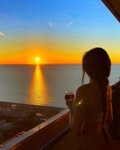 a woman standing on a balcony looking at the sunset at Panorama Sea View Central City Batumi & ApartHOTEL in Batumi
