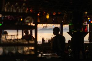 a man sitting at a bar in front of the ocean at JOY Bungalow Resort and Restaurant in Ko Jum