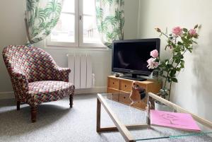 ein Wohnzimmer mit einem TV, einem Stuhl und einem Tisch in der Unterkunft Le Cloître pour 4 personnes in Chartres