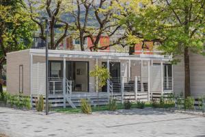 a white house with a porch and trees at Al Lago Camping & Rooms in Riva del Garda