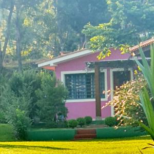 a pink house with a window in a garden at Pousada Villa das Águas,chalés com Ar condicionado e um rio no quintal in Monte Alegre do Sul