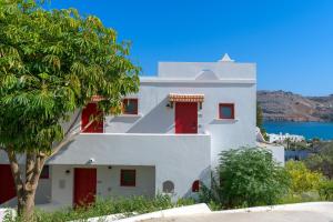 een wit huis met rode deuren en een boom bij Lindos Village Resort & Spa - Adults Only in Lindos