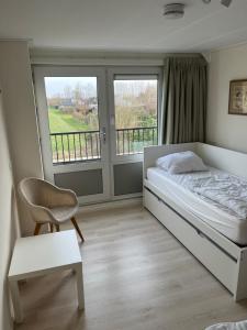 a bedroom with a bed and a chair and windows at La Cabane Penthouse in Nieuwvliet-Bad