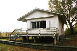 ein kleines weißes Haus mit einer Veranda auf einer Plattform in der Unterkunft Haus am Seeufer mit Veranda in natürlicher Umgebung in Güttingen