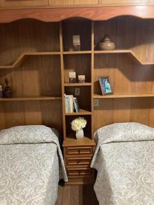 two beds in a bedroom with wooden walls and shelves at Quartos em casa no Clelia Bernardes in Viçosa