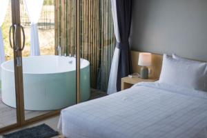 a bedroom with a bed and a tub next to a window at The Chamuang Forest in Ban Dong