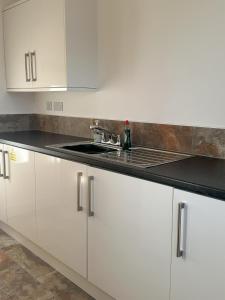 a kitchen with white cabinets and a sink at Whitebridge Cottage in Swansea