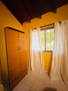 um quarto amarelo com uma janela e cortinas brancas em La carmencita Club de Campo em Ingeniero J. Allan