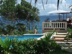 una piscina con sillas y una sombrilla y el océano en Petite Anse Hotel, en Mount Alexander