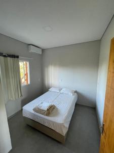 a small bedroom with a bed with white sheets and a window at Vila do Rosa in Praia do Rosa