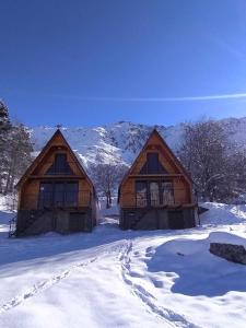 two large wooden buildings in the snow with mountains at Cottage Paradise in Stepantsminda