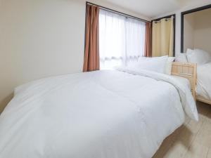 uma grande cama branca num quarto com uma janela em 一棟貸しの民泊いとんちゅ em Nagasaki