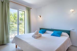 een slaapkamer met een wit bed met blauwe kussens en een raam bij Cala Mendia Beach House 1 by Slow Villas in Cala Romantica