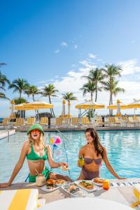 duas mulheres de biquíni sentadas numa mesa numa piscina em Newport Beachside Hotel & Resort em Miami Beach