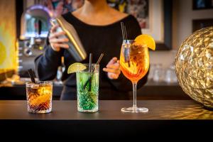 een vrouw zit aan een bar met drie cocktails bij Hôtel Quorum in Saint-Cloud