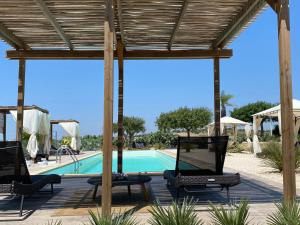 a swimming pool with two chairs and a wooden pergola at Scilla Maris Charming Suites in Marzamemi