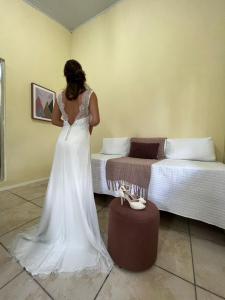 Eine Frau in einem Hochzeitskleid, die neben einem Bett steht. in der Unterkunft Sítio Colina Eventos in Santo Antônio do Rio das Pedras