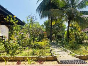 a garden with a pathway and a palm tree at Harmony Beach Hotel in Arugam Bay
