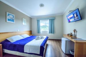 1 dormitorio con 1 cama azul y TV en Pousada Parque das Flores, en Campos do Jordão